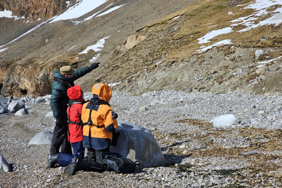 expedition-leader-john-rodsted-pointing-to-the-arctic-fox-fjortende-julibukta-mette-eliseussen-2024-secret-atlas