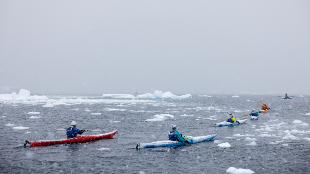 A group of kayakers in a line in snowy icy waters