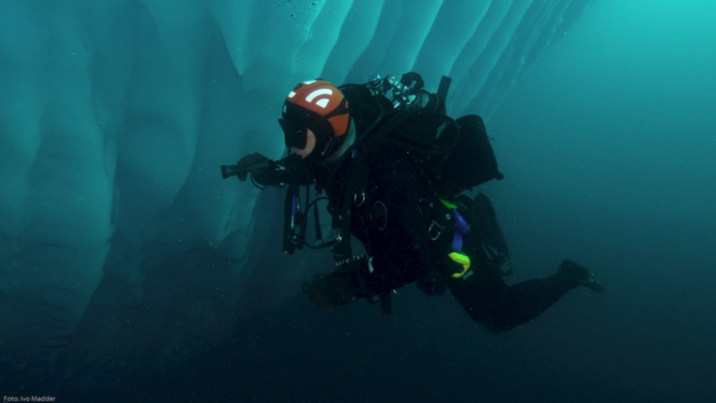 A person scuba dives alongside an iceburg